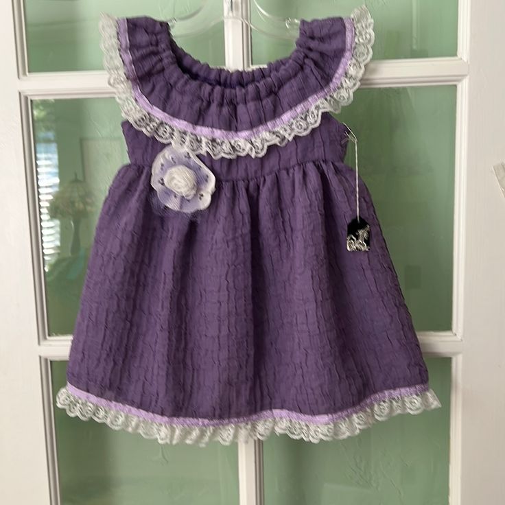 New Purple Handmade Sleeveless Dress. Lace And Ribbon Have Been Sewn Around The Ruffle On The Neck And Hem. A Handmade Lace Rose Has Been Added To The Front Of The Dress. Purple Sleeveless Dress For Spring Dress-up, Purple Sleeveless Dress For Dress-up, Sleeveless Sundress For Playtime, Cute Sleeveless Sundress For Playtime, Cute Purple Sleeveless Sundress, Cute Purple Sleeveless Dress, Cotton Sleeveless Sundress For Babies, Sleeveless Ruffled Sundress For Playtime, Sleeveless Ruffled Sundress For Dress-up