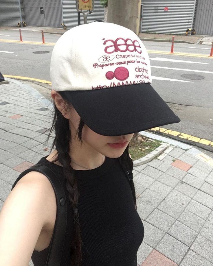 a woman wearing a black and white hat standing on the side of a city street