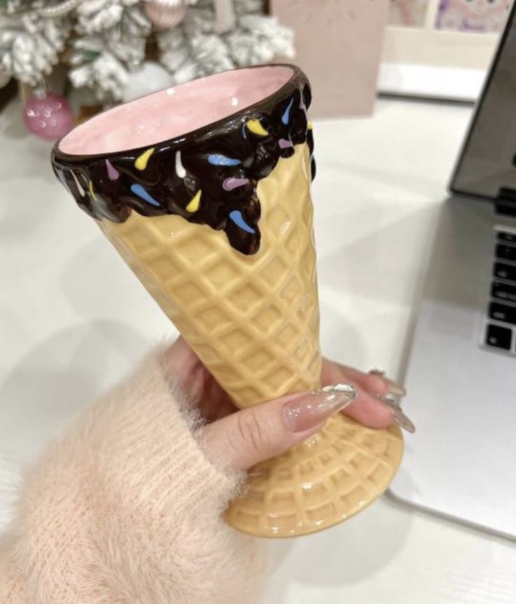 a hand holding an ice cream cone with chocolate on top and sprinkles