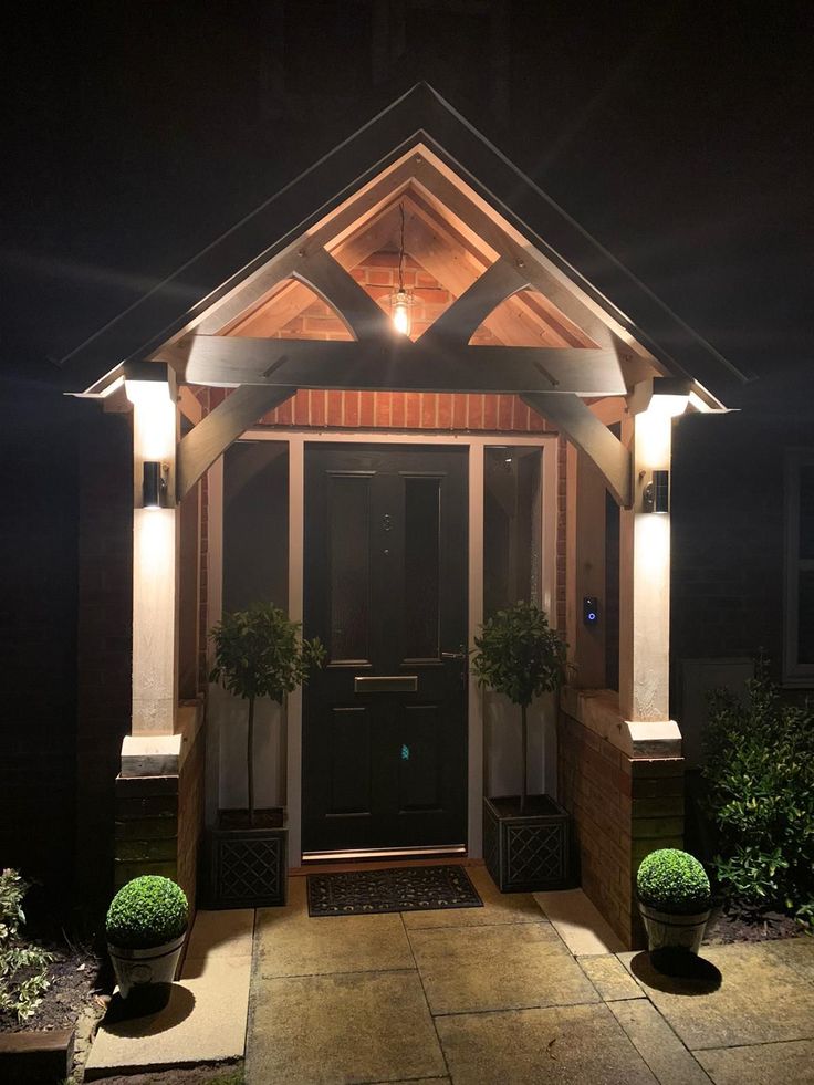 a lit up entrance to a house at night with potted plants on either side