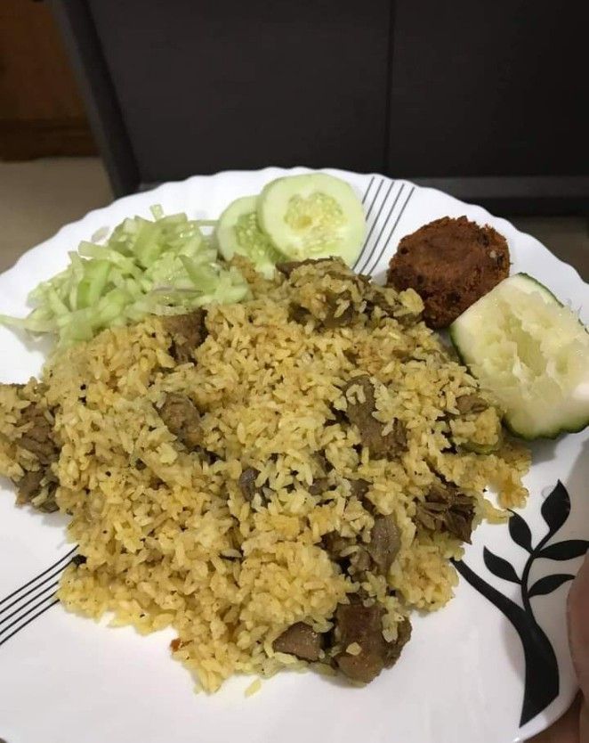 a white plate topped with rice and meat next to cucumbers on a table