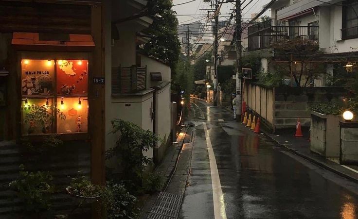 an alley way with buildings and lights on the side, in the rain at night