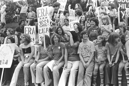 a group of people sitting on top of each other in front of a crowd holding signs