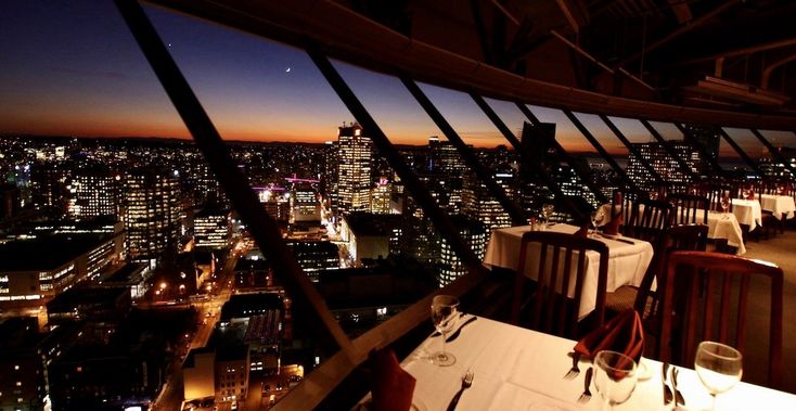 a restaurant overlooking the city at night with tables and chairs set up for dinner in front of large panoramic windows