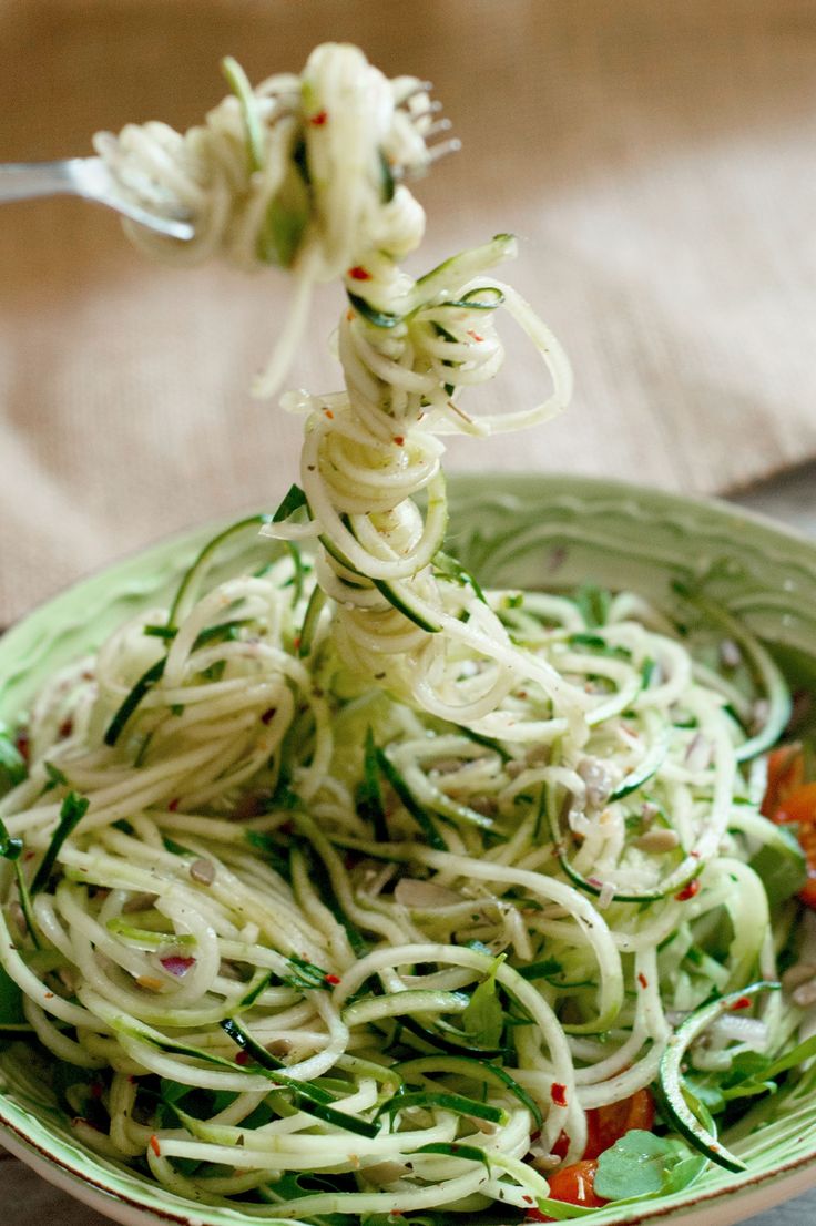 a bowl filled with noodles and vegetables on top of a wooden table next to a fork