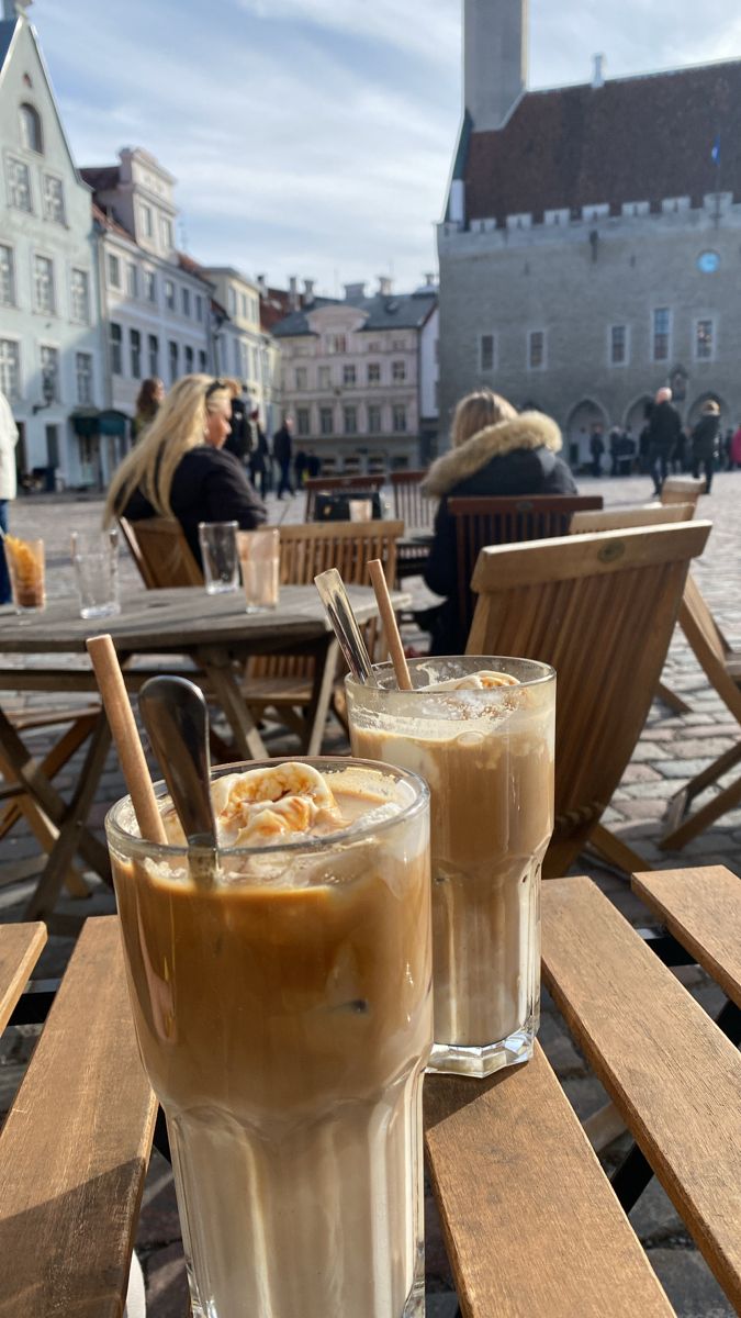 two drinks sitting on top of a wooden table in front of some people and buildings