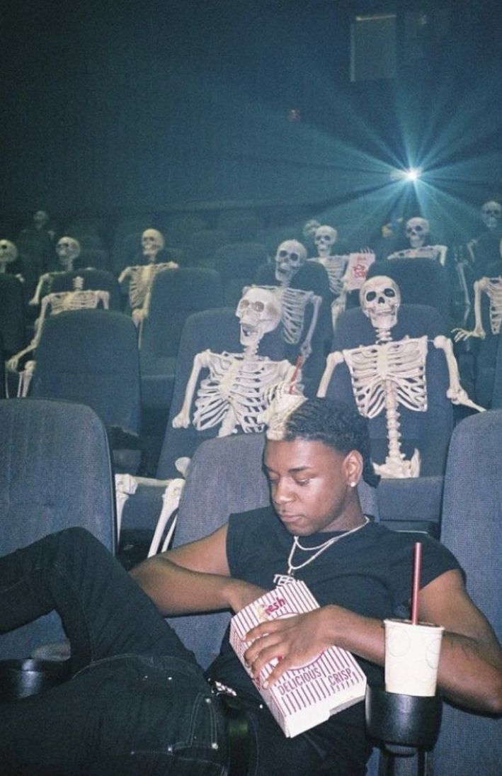 a man sitting in a movie theater with skeletons behind him