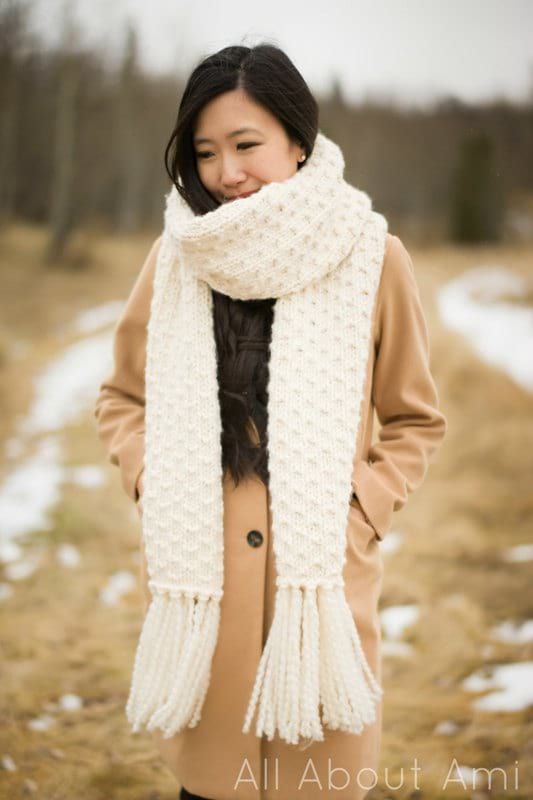 a woman standing in the snow wearing a white scarf and coat with her hands on her hips