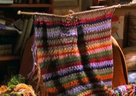 a multicolored crocheted blanket sitting on top of a wooden chair next to a pile of books