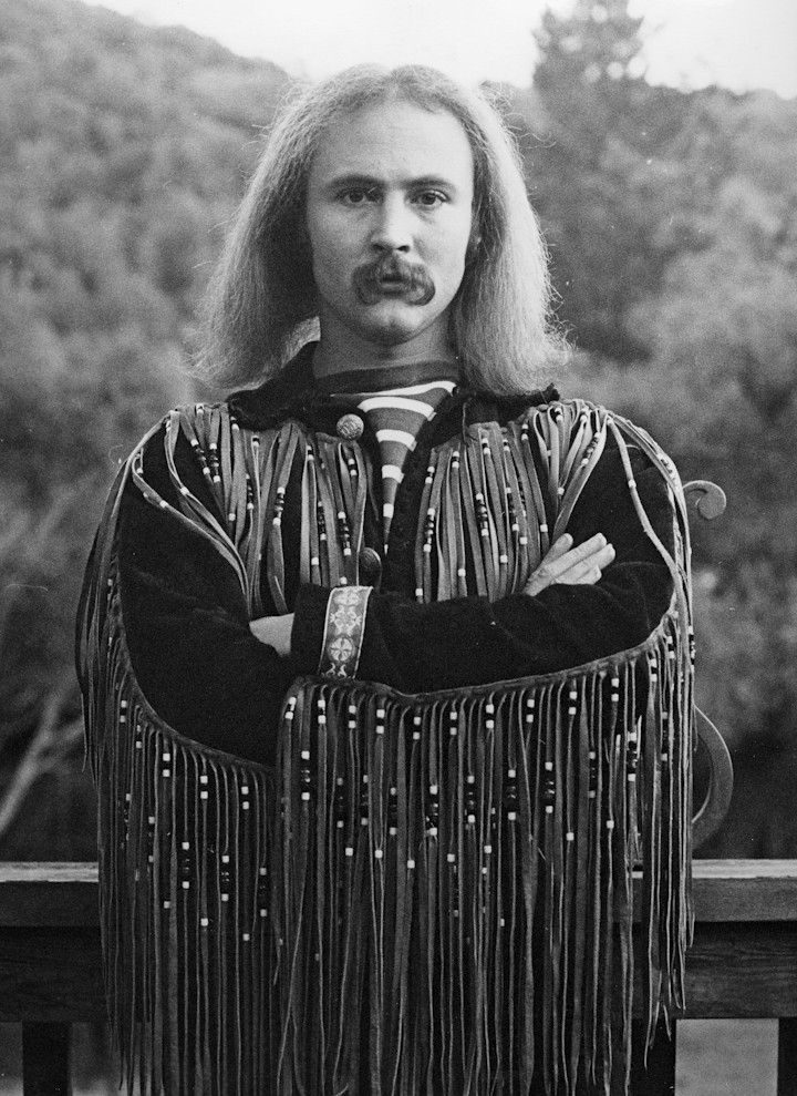 an old photo of a man with long hair wearing a fringe jacket and holding his arms crossed