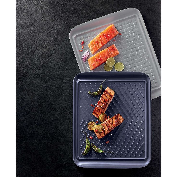 two trays with food on them sitting on a black counter top next to each other