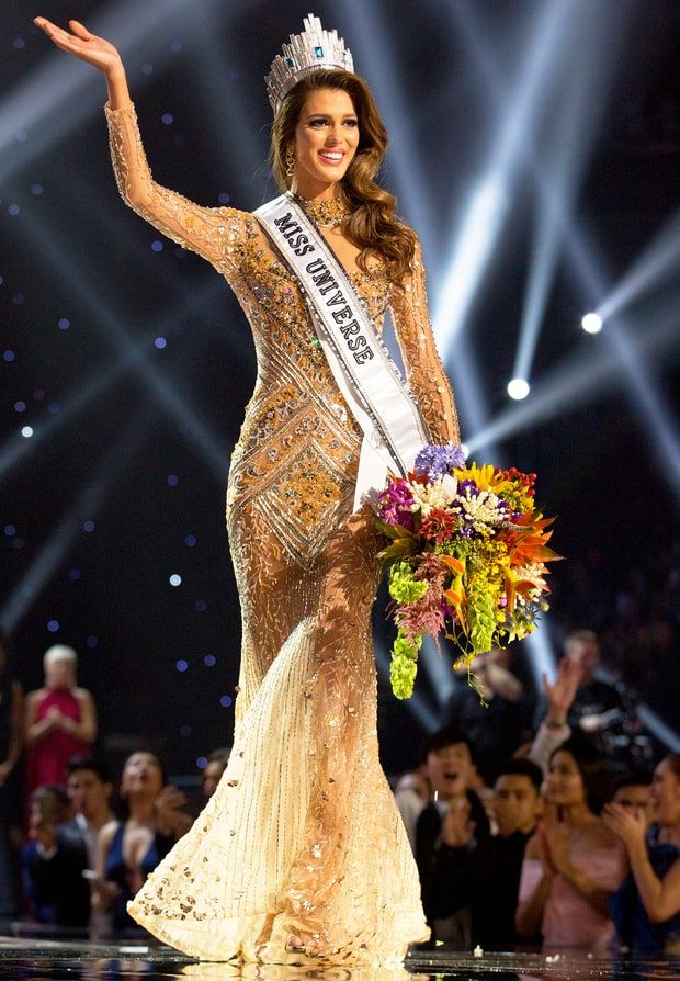 a woman in a gold gown and crown waves to the crowd as she walks on stage