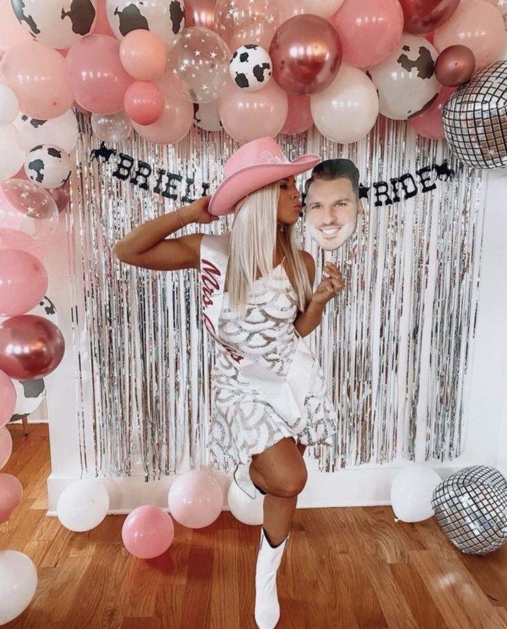 a woman in a white dress and pink hat posing for a photo with balloons behind her