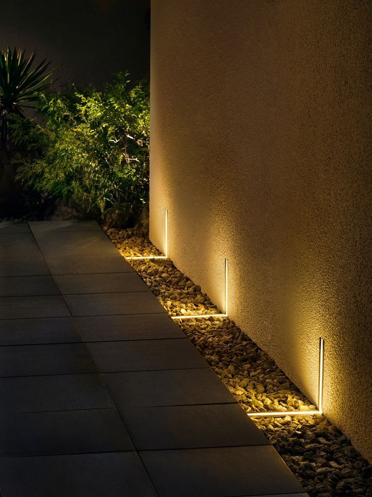 an outdoor walkway lit up at night with lights on the side and plants in the background