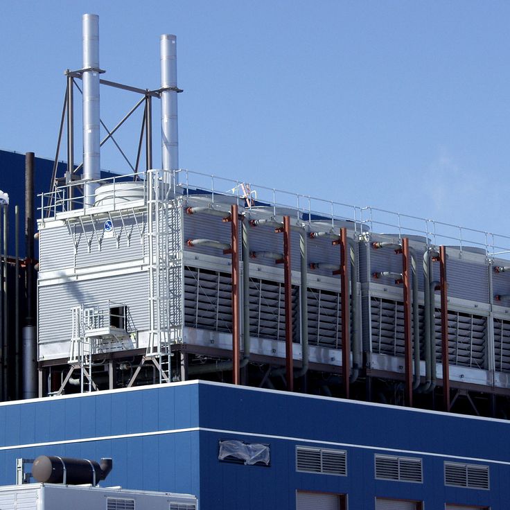 an industrial building with large pipes and cooling towers on top, against a clear blue sky