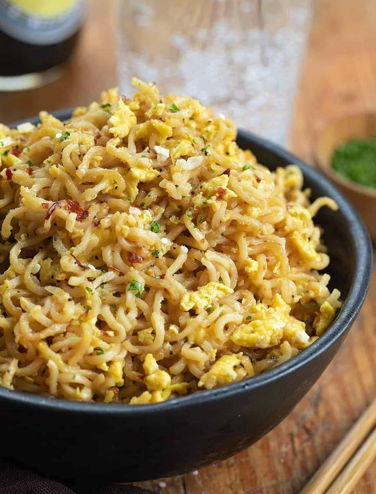 a black bowl filled with noodles on top of a wooden table