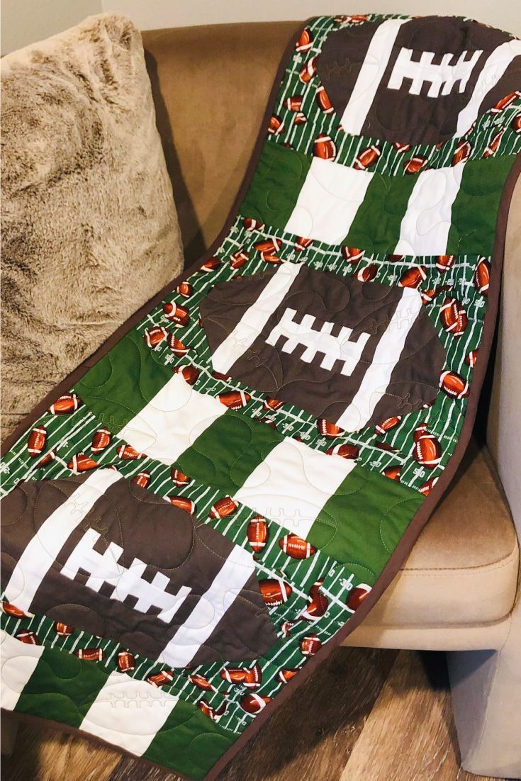 a green and white quilted football blanket on a couch next to a brown pillow