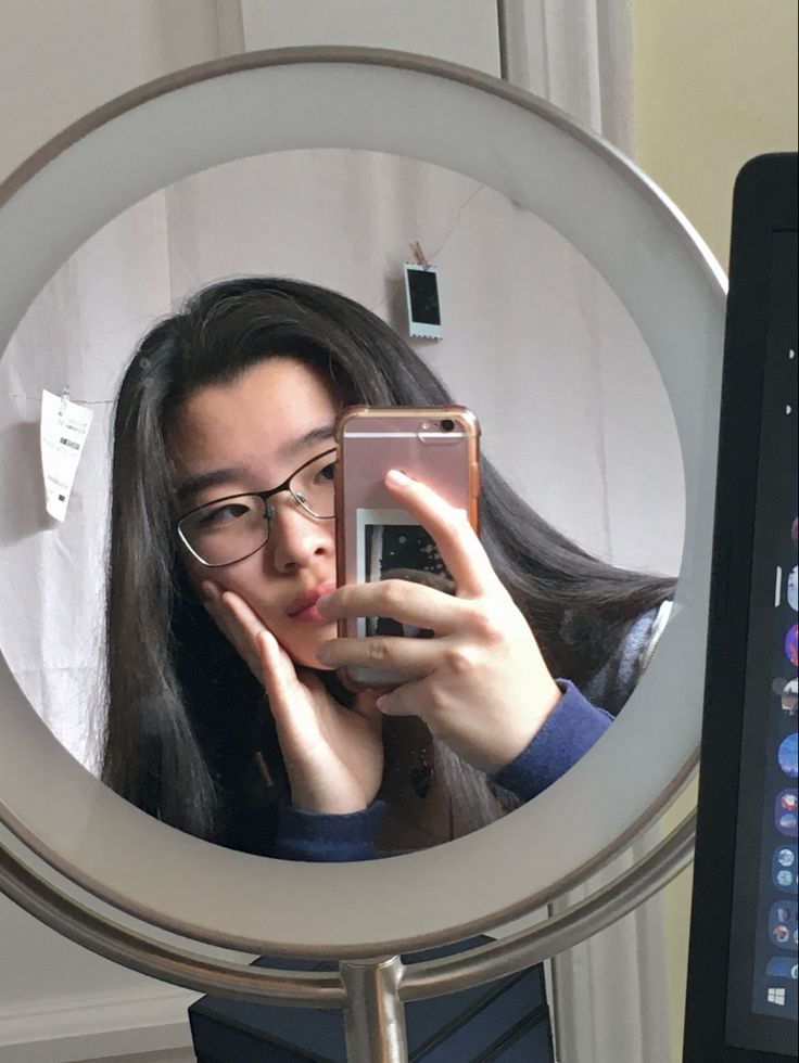 a woman taking a selfie with her cell phone in front of a circular mirror