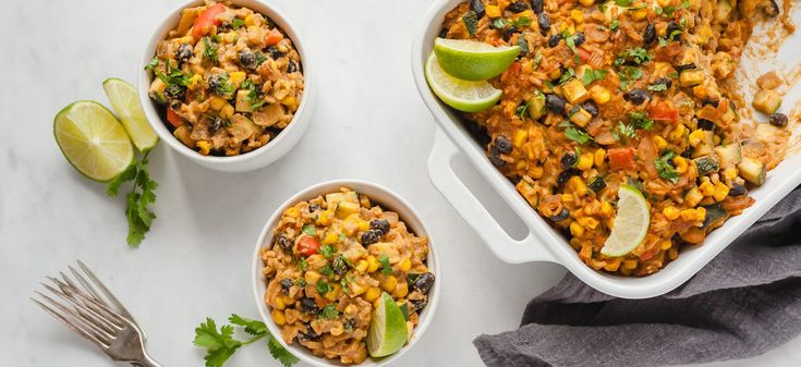 two bowls filled with mexican food next to a fork and lime wedges on the side