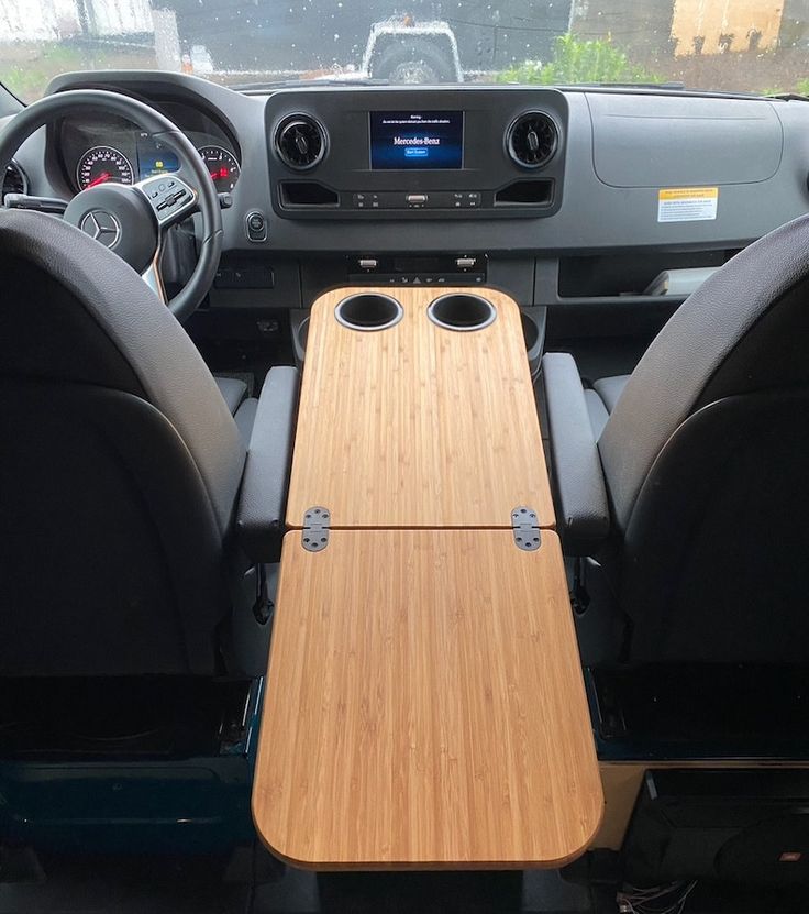 the interior of a vehicle with a wooden table in the center and two black seats