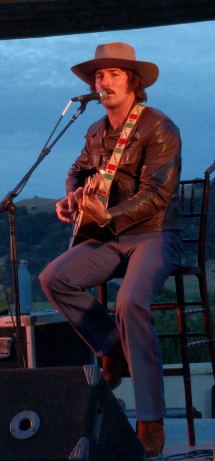 a man with a hat and guitar on stage