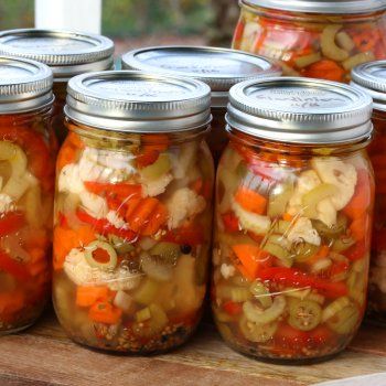 several jars filled with pickled vegetables sitting on top of a wooden table