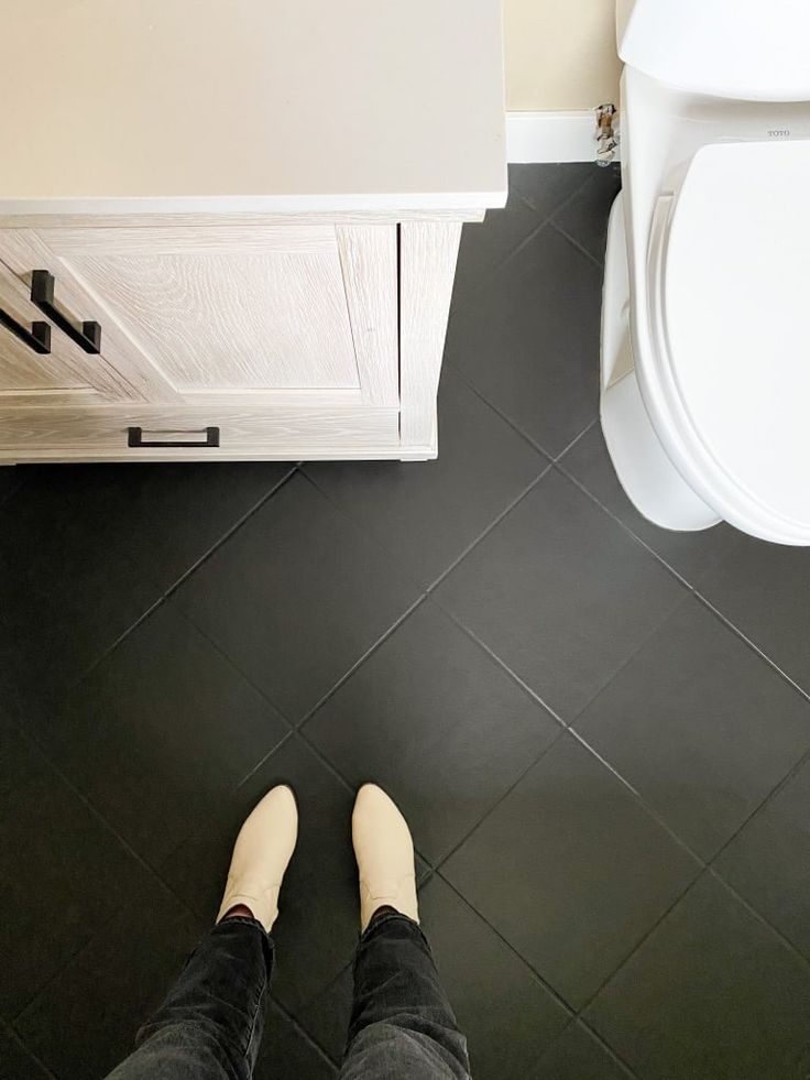 a person standing in front of a white toilet next to a black tile bathroom floor