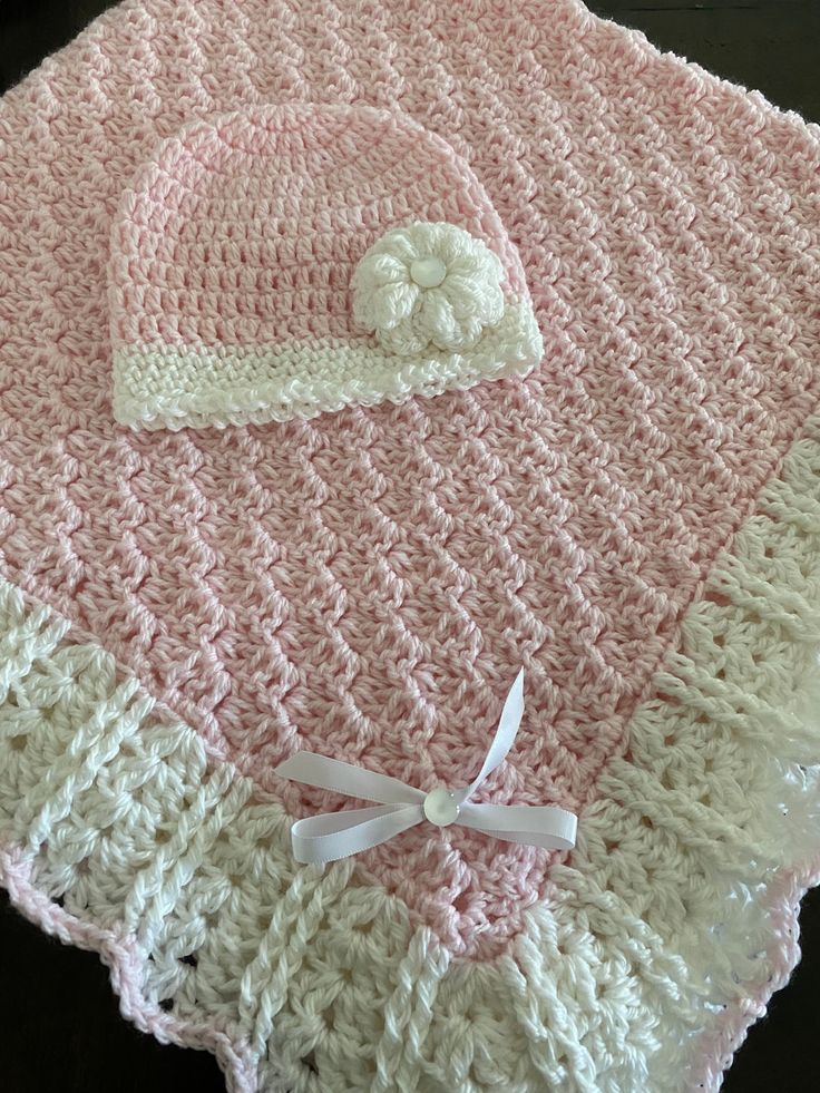 a pink and white crocheted baby blanket with a hat on it's top