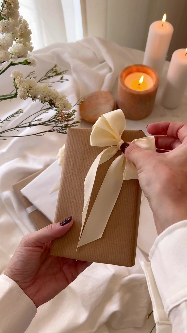 a woman holding a gift box with a bow on it and candles in the background