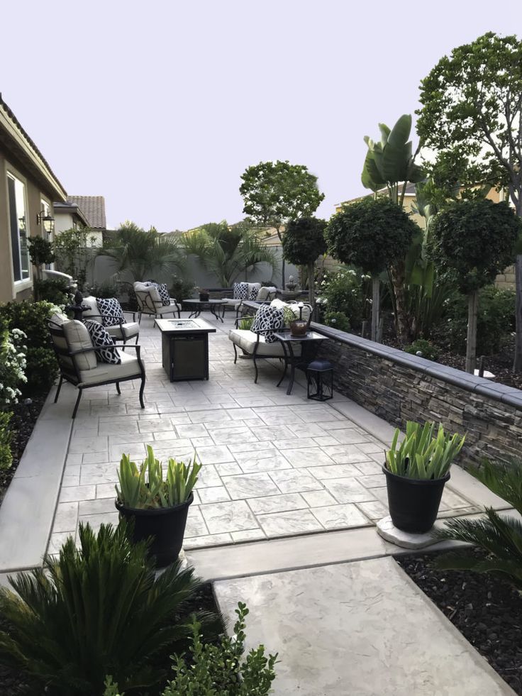 an outdoor patio with chairs and tables surrounded by trees, shrubs and plants on either side of the walkway