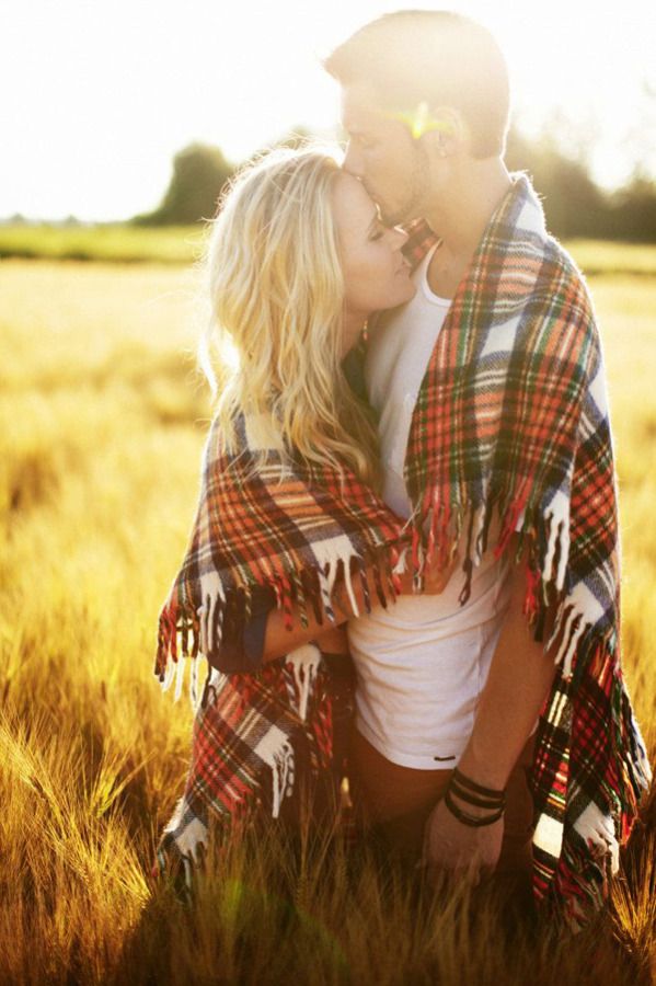 two people are kissing in the grass and one person is wearing a plaid blanket while the other has a white shirt