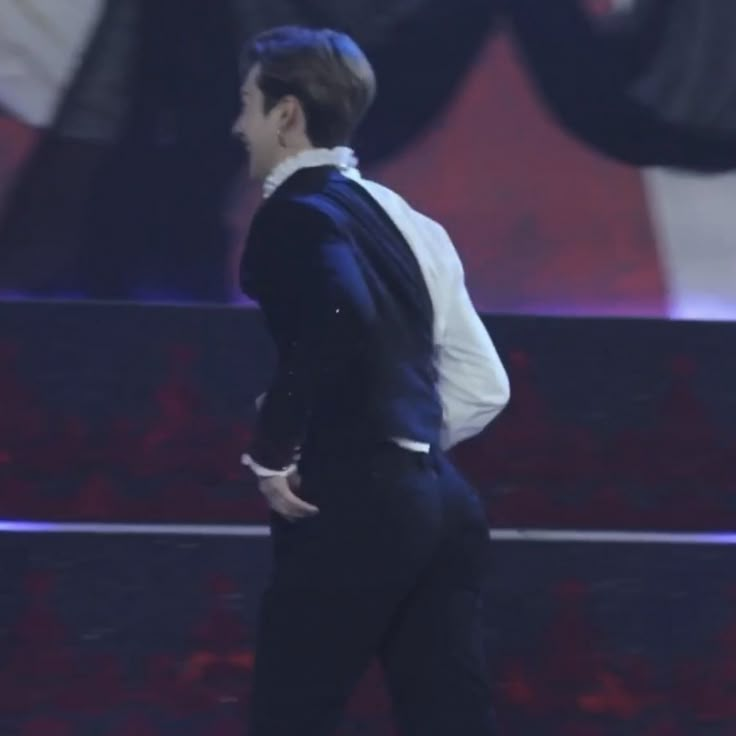 a male in a black suit and white shirt is walking down the stage with his hand on his hip