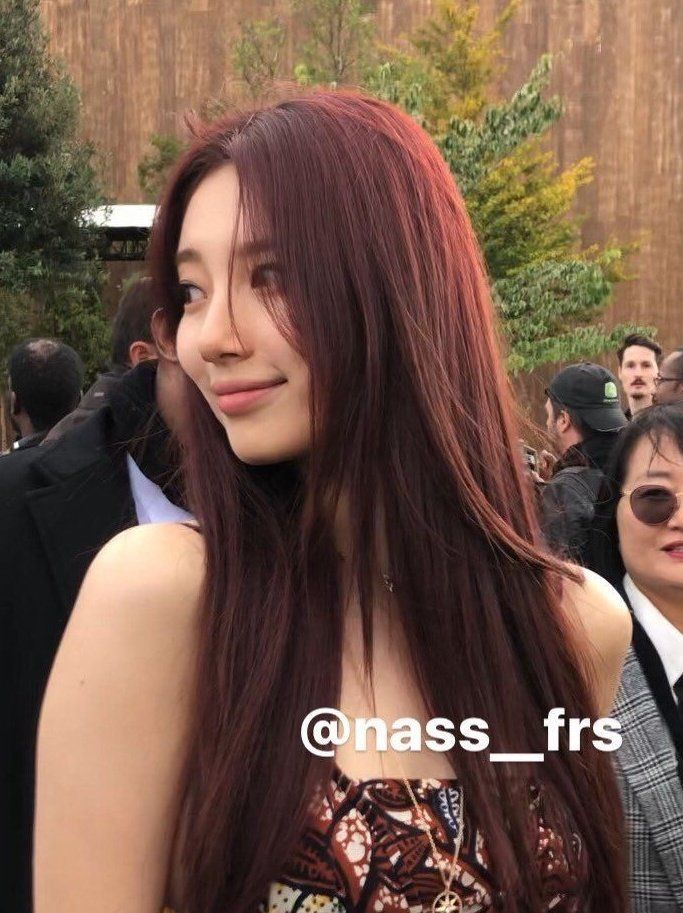 a woman with long red hair standing in front of a group of people at an event