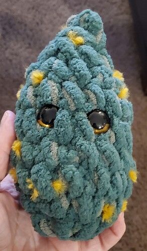 a hand holding up a crocheted stuffed animal with yellow and black dots on it's eyes