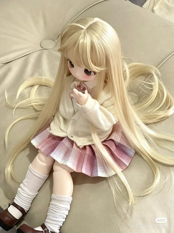 a doll with long blonde hair sitting on a bed