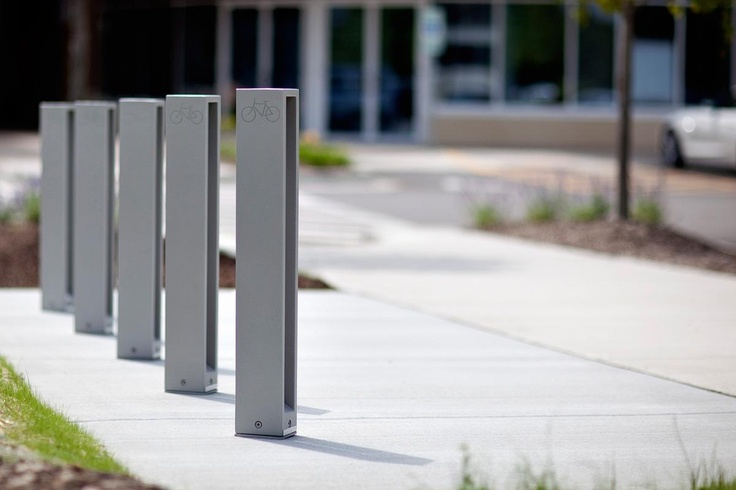 four metal posts are lined up on the sidewalk near grass and trees in front of a building