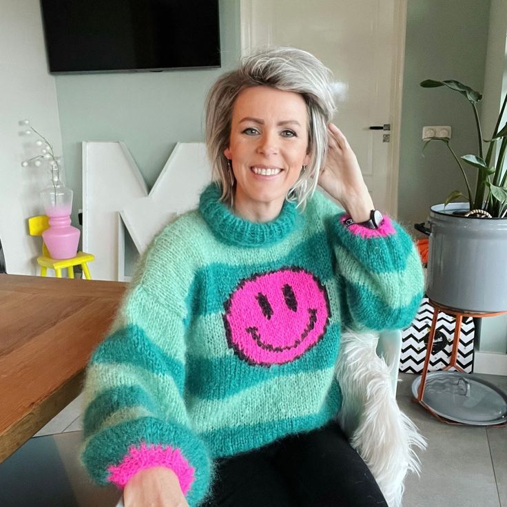 a woman sitting in a chair wearing a green sweater with pink smiley face on it