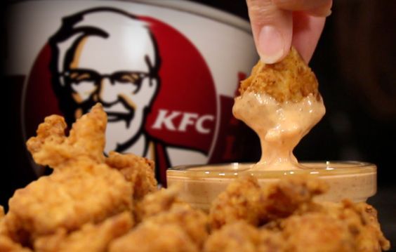 a person dipping some kind of food into a container with kfc's logo in the background