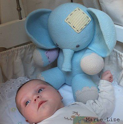 a baby laying in a crib next to a blue stuffed elephant and teddy bear