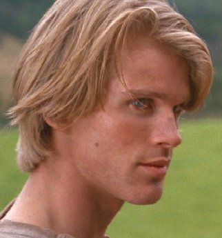 a close up of a person in a field with green grass and trees behind him