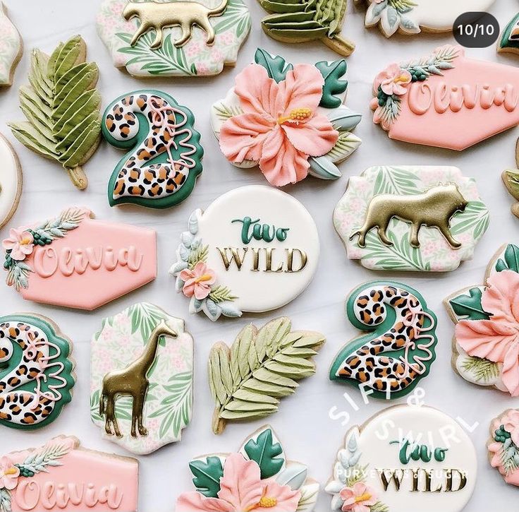 some decorated cookies are laying out on a white surface with pink and green flowers, leaves, and giraffes