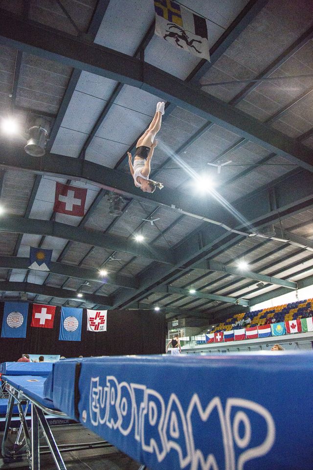 a man flying through the air while riding a skateboard in a gym with other people watching