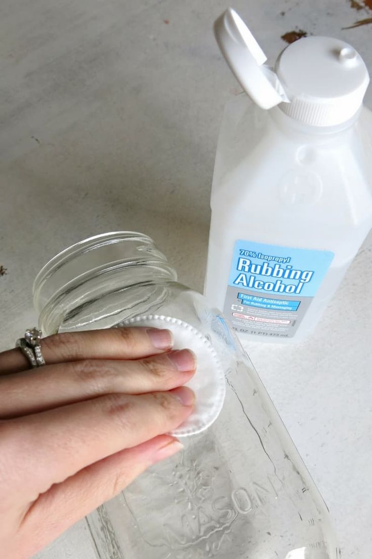 a person's hand is holding a glass jar next to a bottle of water