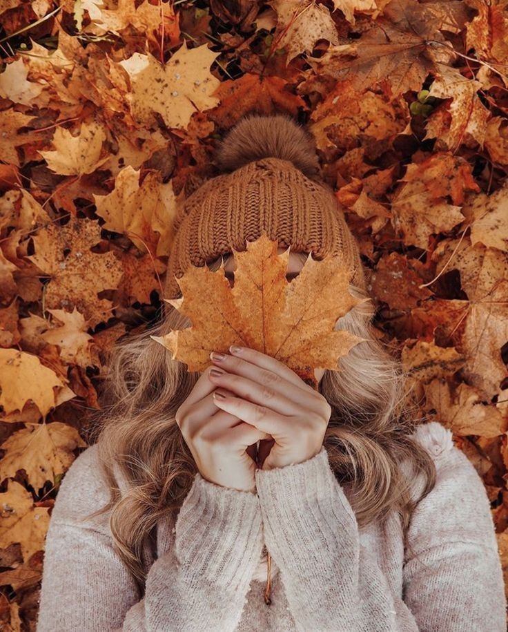 a woman covering her face with an autumn leaf