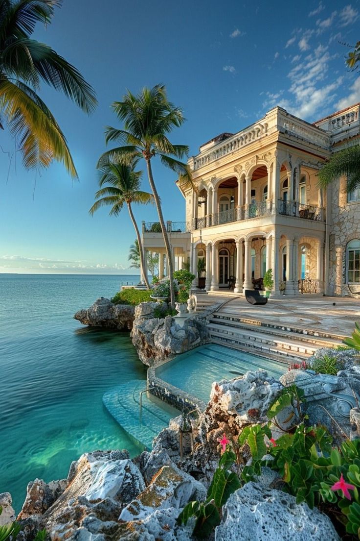 a large house sitting on top of a lush green hillside next to the ocean with palm trees