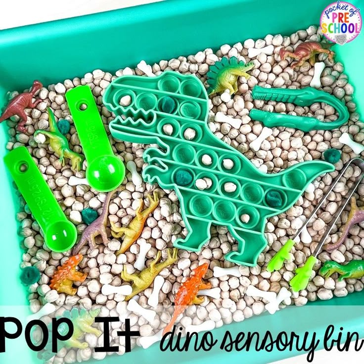 a green tray filled with lots of toys and rocks in the shape of a dinosaur