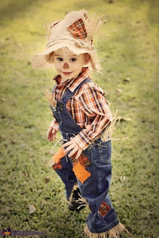 a little boy wearing a hat and overalls standing in the middle of a field