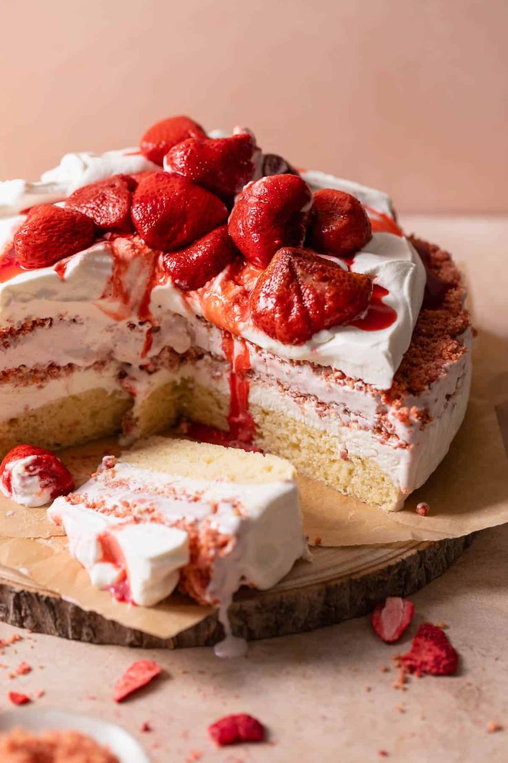 a cake with strawberries on top is cut into pieces and sits on a cutting board