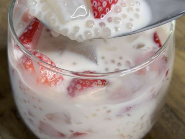 strawberries and milk are mixed together in a glass with a spoon on a wooden table