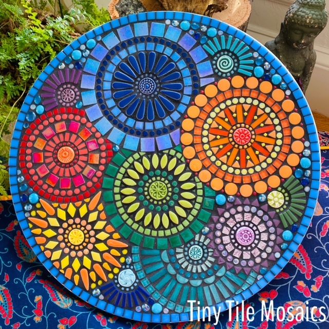 a colorful plate sitting on top of a table next to a vase and potted plant